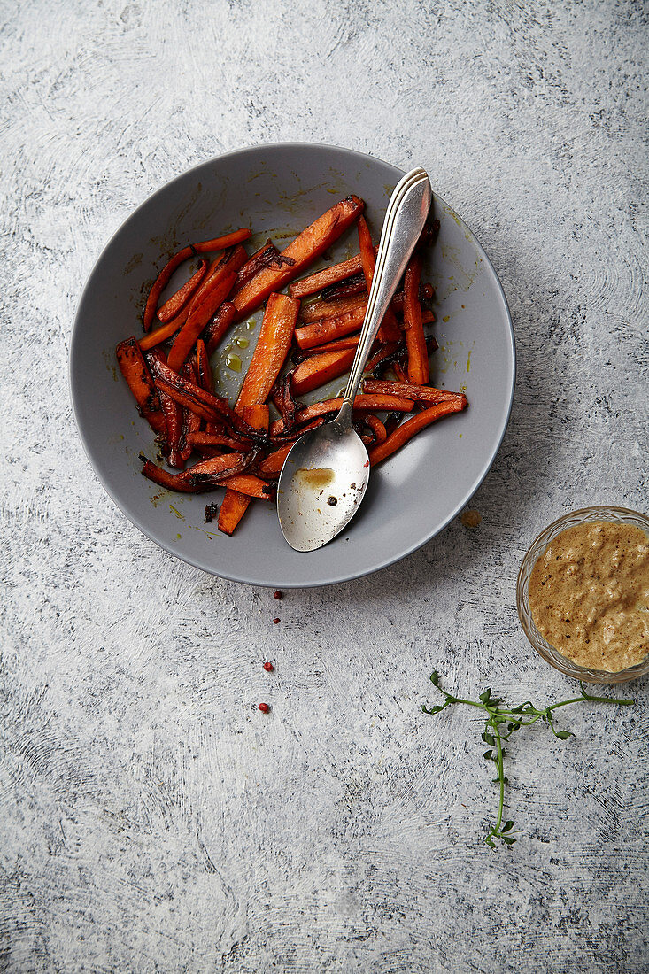 Flatlay image with roasted caramelized carrots with olive oil and honey sauce in gray bowl on textured background