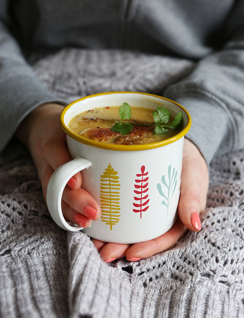 Vegetable soup in mug topped with croutons and fresh coriander