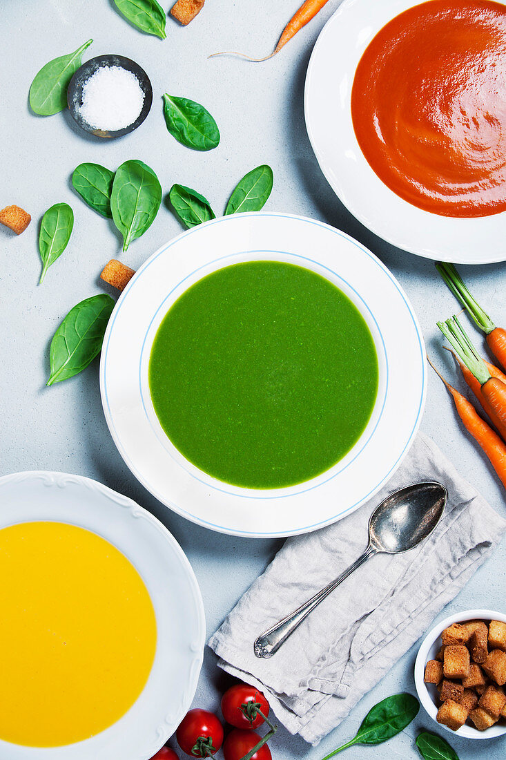Pumpkin, tomato and spinach soups over grey concrete background