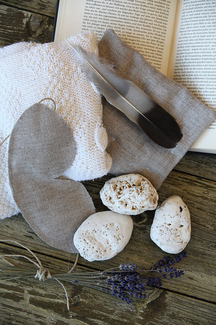 Still-life arrangement of limestone pebbles, lavender, sleeping mask, heat cushion and feather