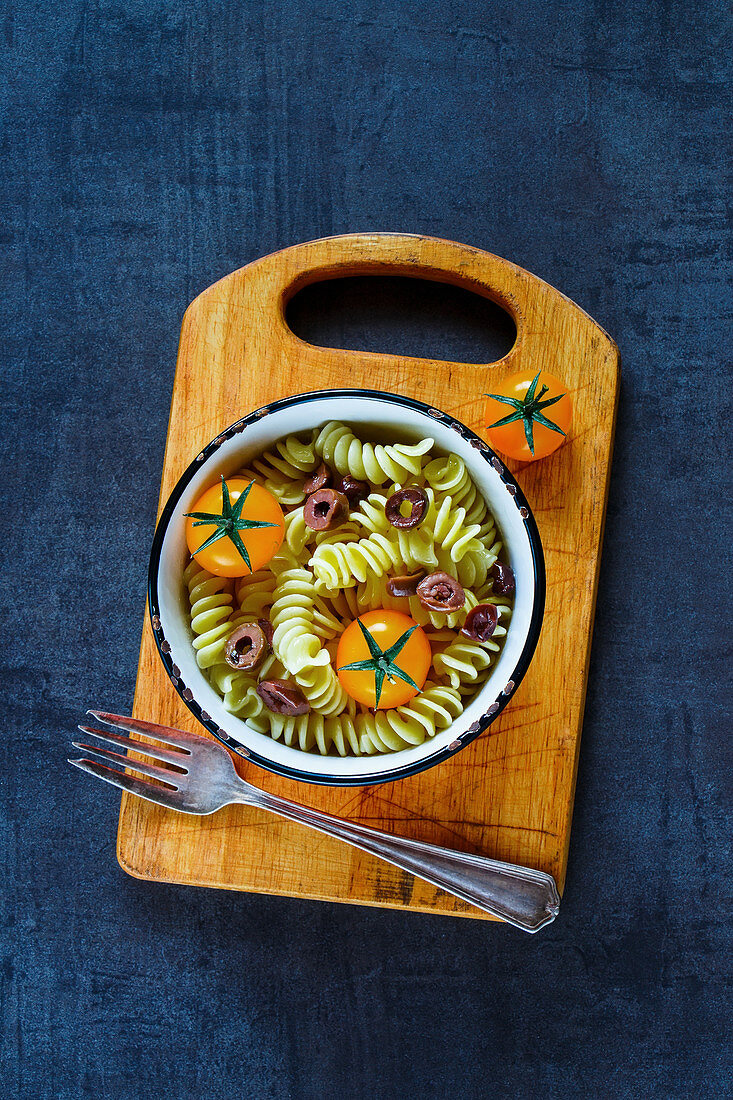 Food background with tasty light pasta salad, fresh raw tomatoes and olives in vintage bowl over grunge table