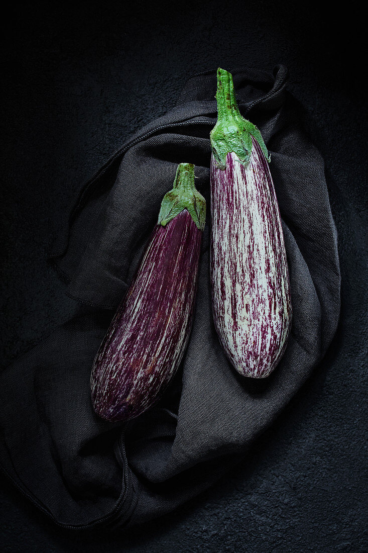 Two aubergines on a black cloth