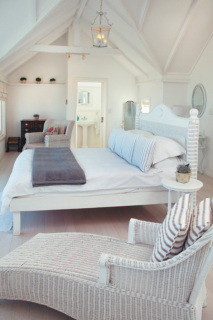 Wicker armchair and bed in white attic bedroom