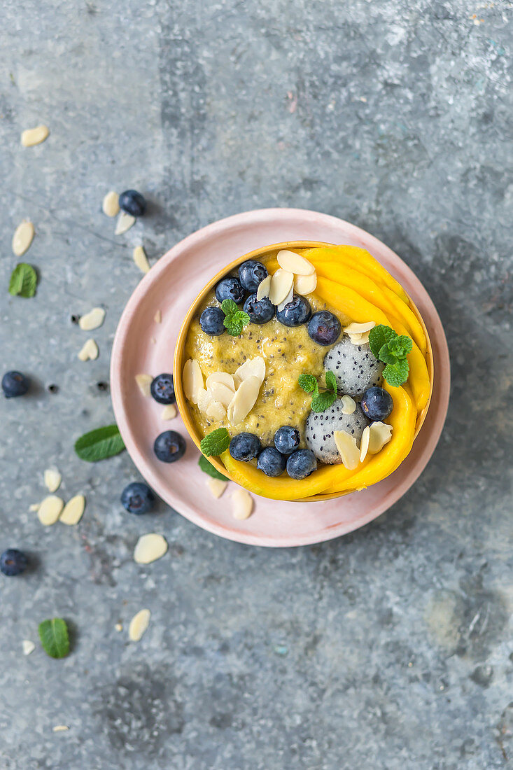 Mango and chia smoothi bowl decorated with mango slices, blueberry, pitaya and almond flakes
