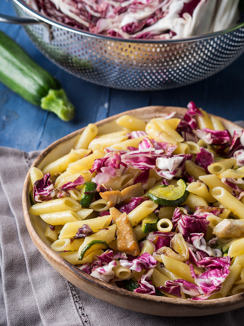Pennette pasta with red chicory, zucchini and grilled chicken in a rustic bowl