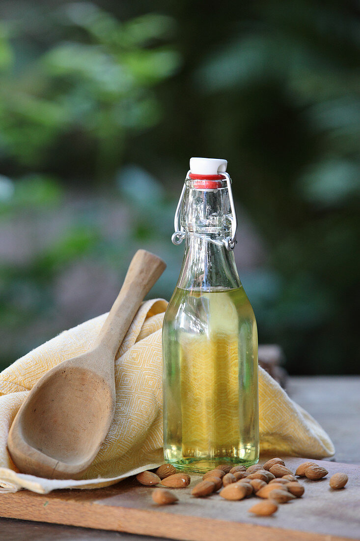 Mandelöl in einer Bügelflasche und Mandeln auf Holztisch