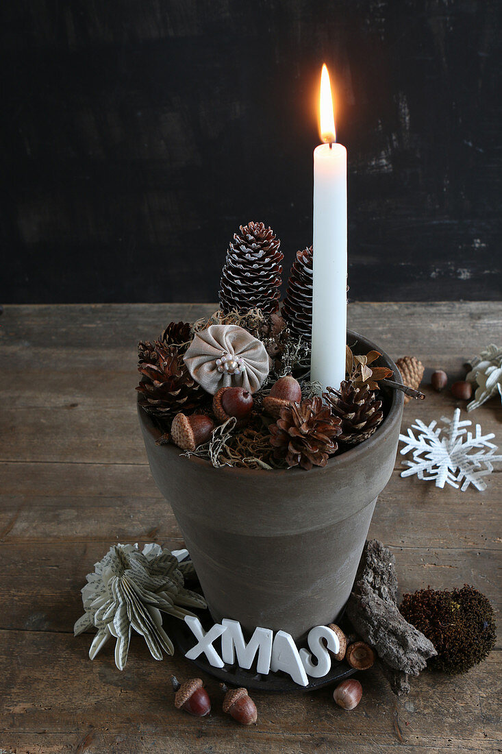 Lit candle in clay pot with festive decorations