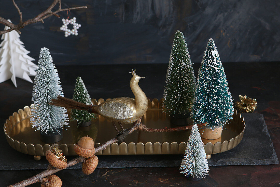 Peacock figurine on twig in front of Christmas tree ornaments on tray