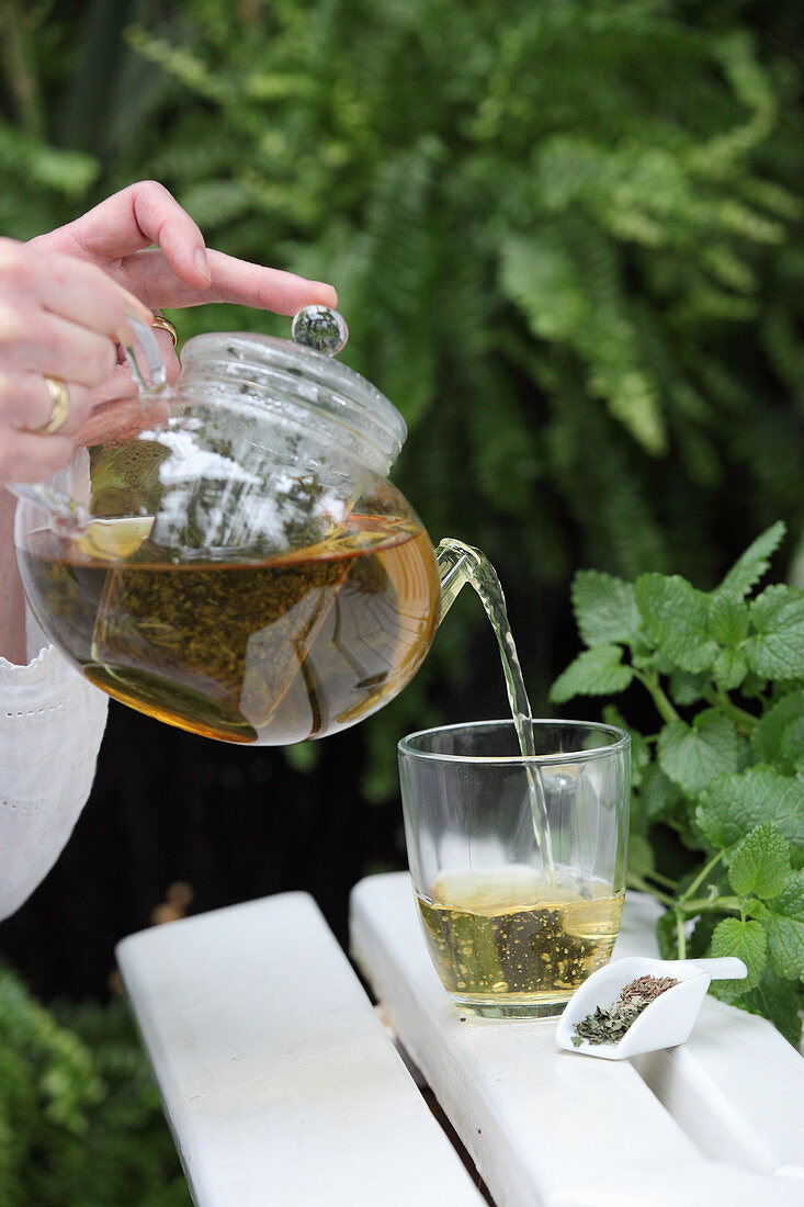 Herbal tea against nausea being poured from a glass teapot into a glass cup