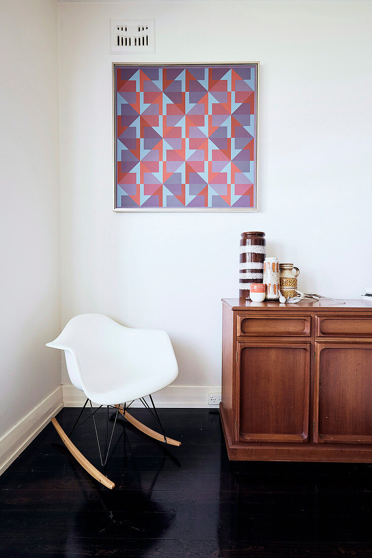 Rocking chair in front of an old sideboard under the graphic painting