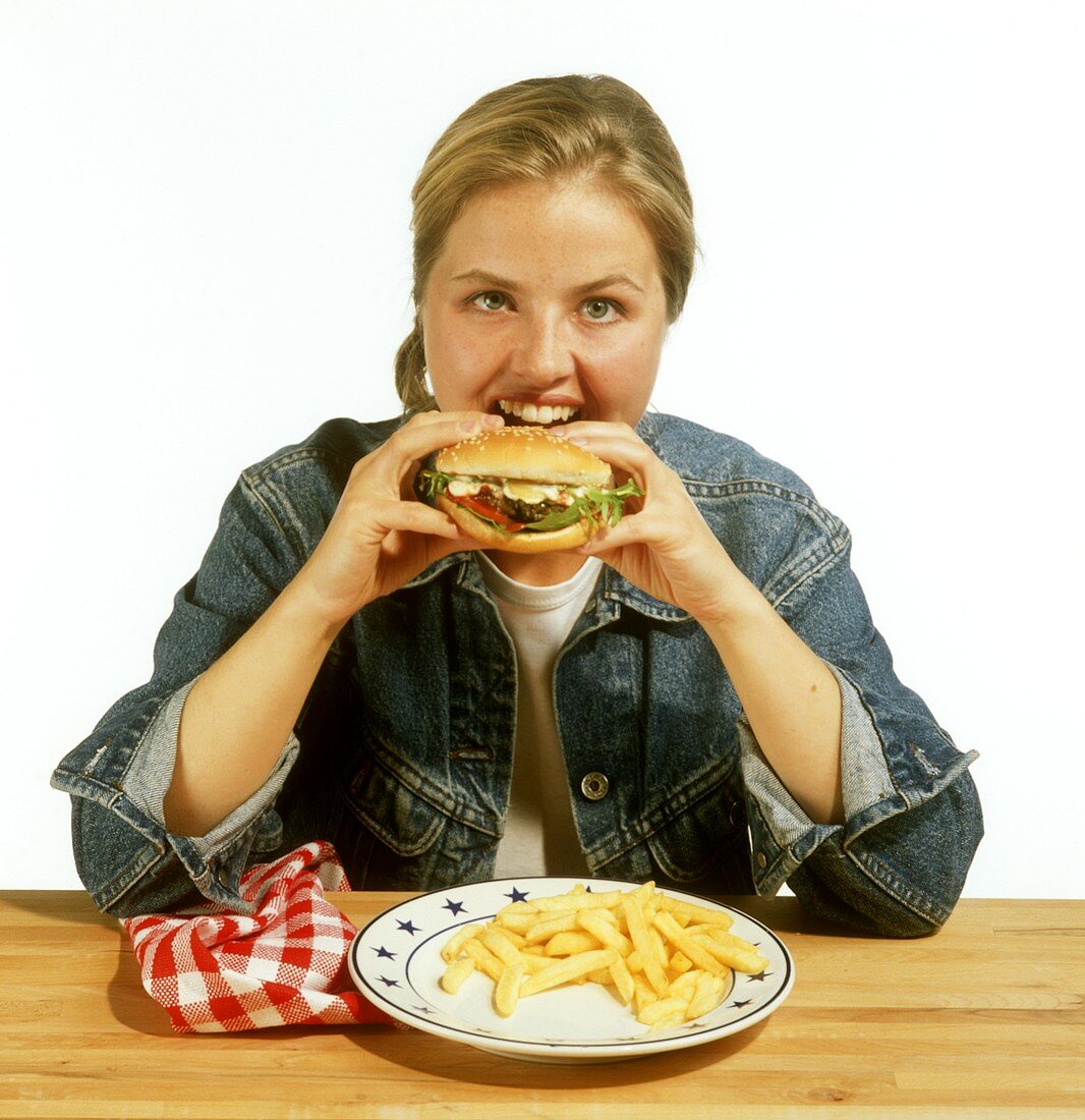 Modell frisst einen Hamburger (am Tisch mit Pommes auf Teller)
