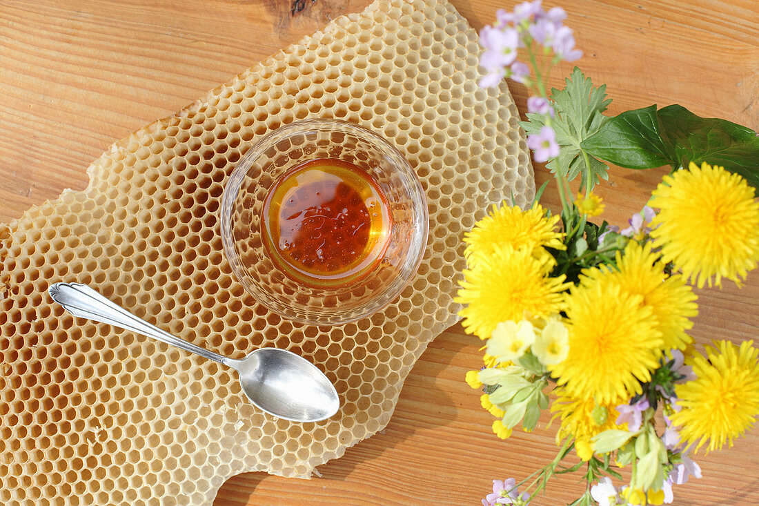 A bowl of honey on honeycomb and a bunch of meadow flowers