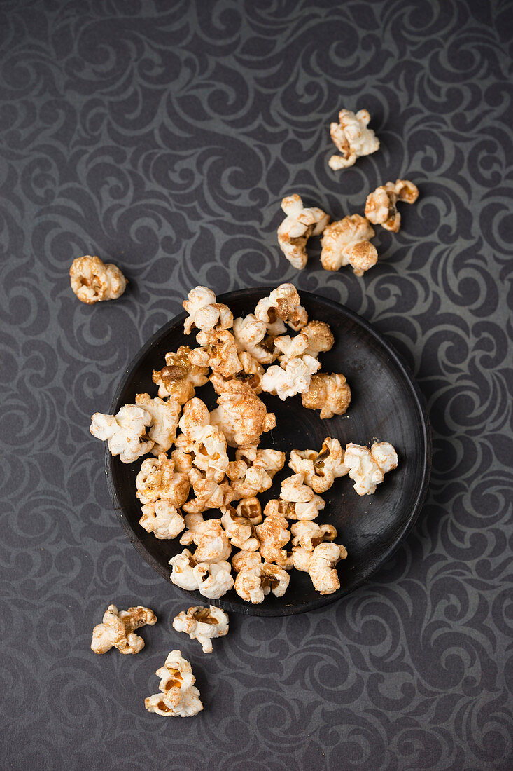 Vergoldetes Popcorn auf Teller und gemusterter Tischdecke (Aufsicht)