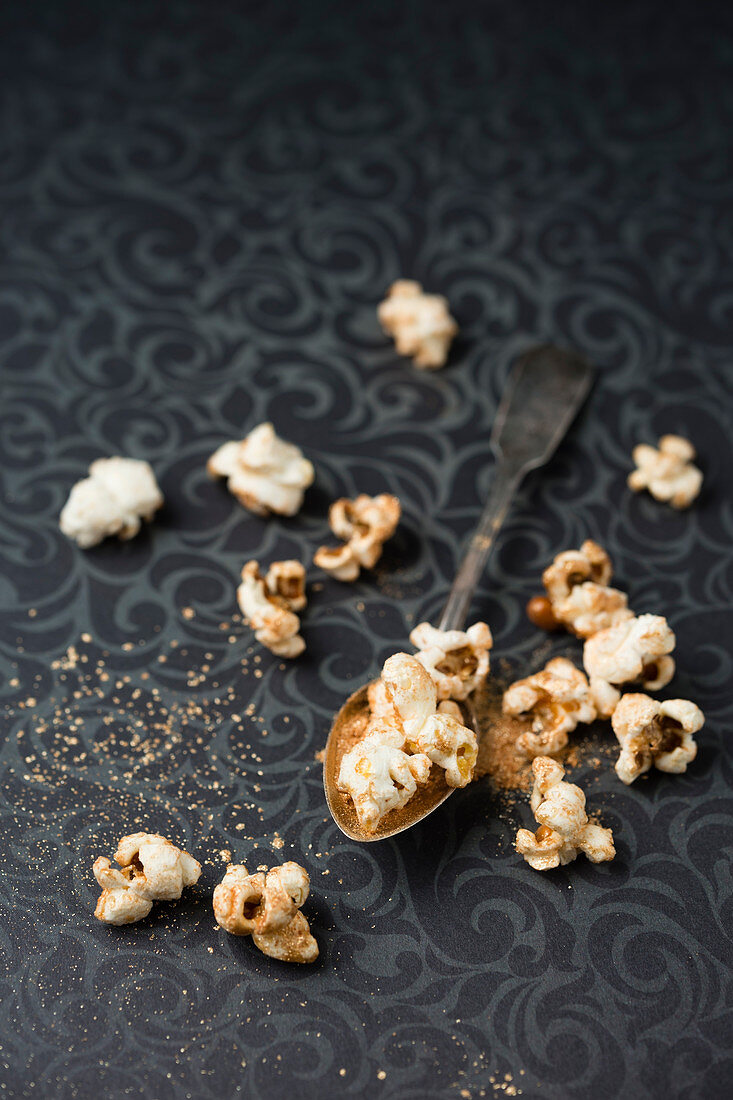 Vergoldetes Popcorn auf Löffel und gemusterter Tischdecke