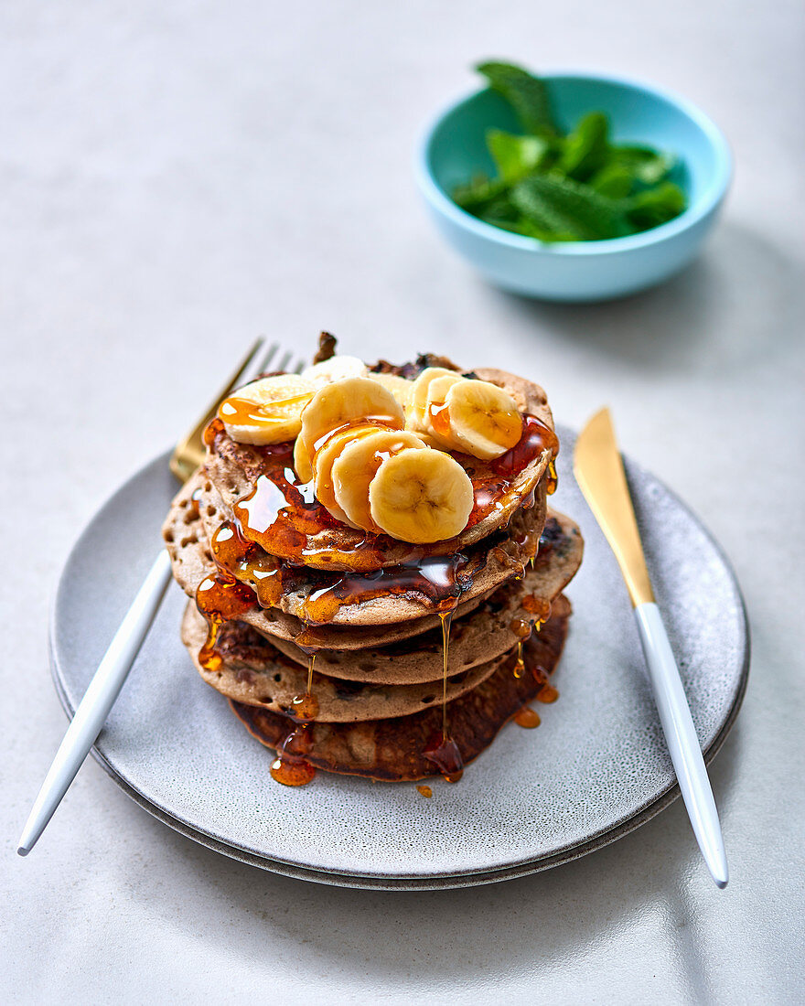 A stack of buckwheat pancakes with blueberries, bananas and syrup