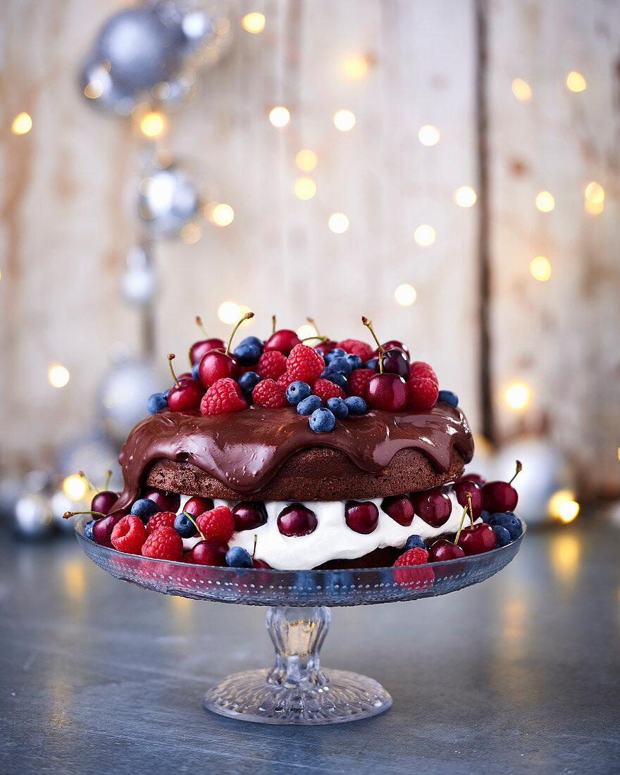 A festive chocolate cake with cream and ganache, decorated with berries and cherries