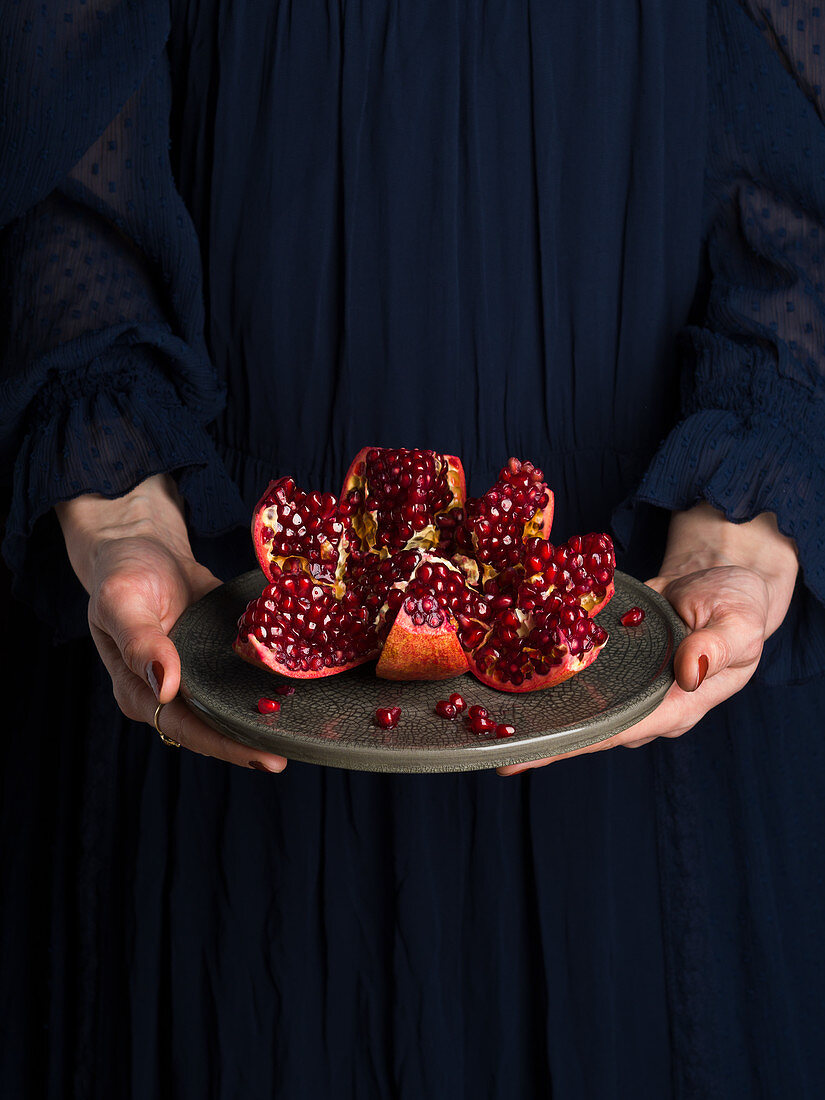 Woman in blue dress holding a dish with open red pomegranate