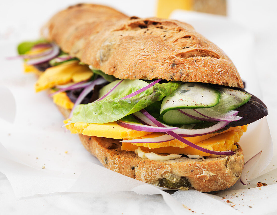 Baguette-Sandwich belegt mit Käse, Zwiebeln, Gurke und Salat
