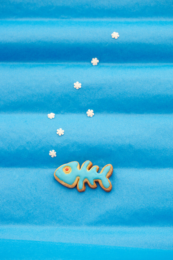 Ein Keks in Fischform mit blauer Zuckerglasur auf blauem Untergrund