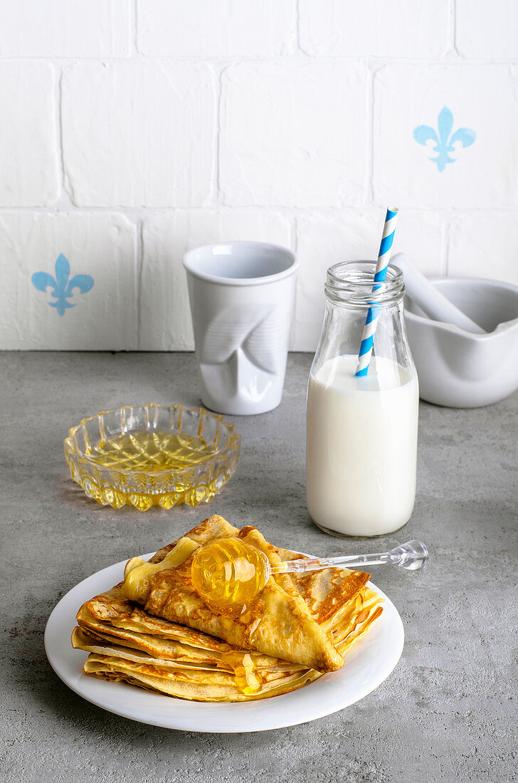 Ukrainian thin pancakes with honey stacked in a pile on a concrete background