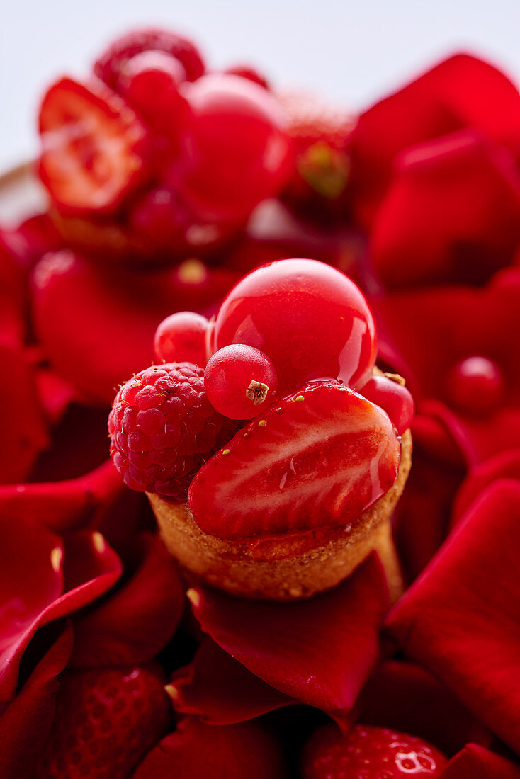 Törtchen mit roten Früchten auf Rosenblütenblättern und roten Beeren