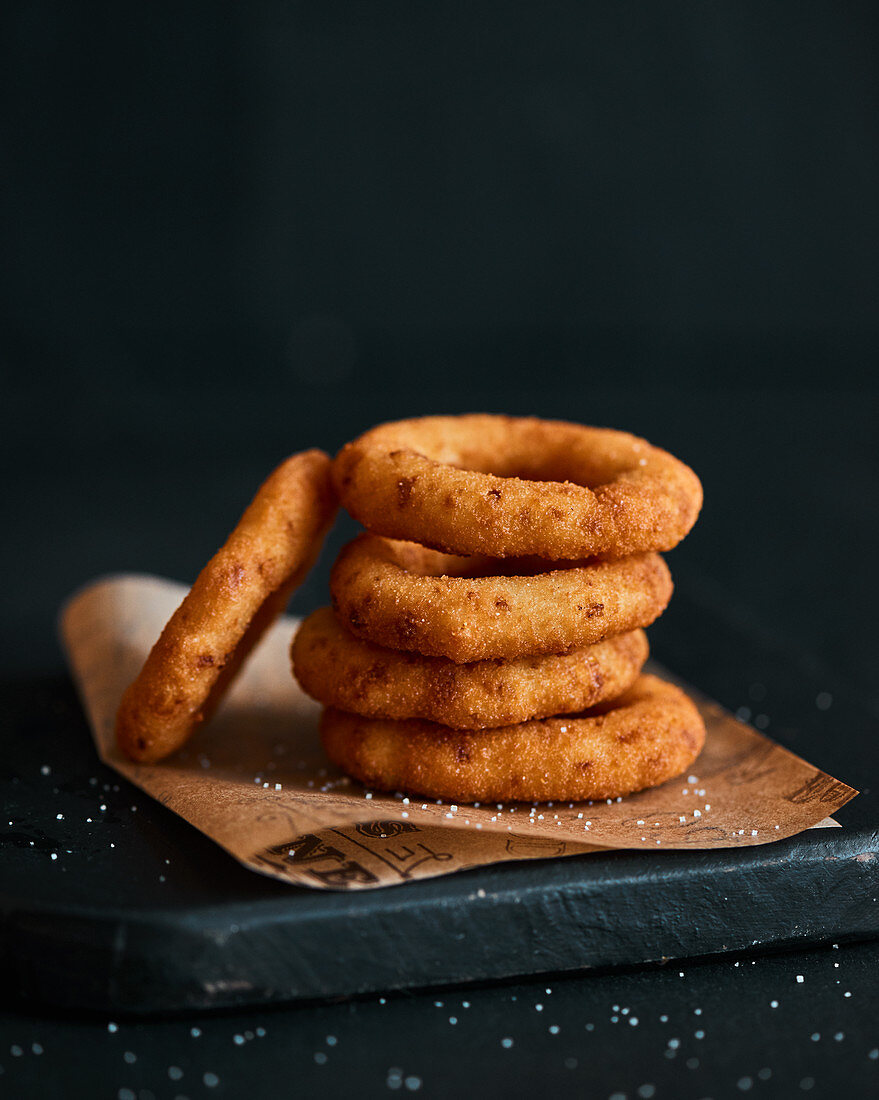 Deep-fried onion rings, sprikled with salt in a dark mood