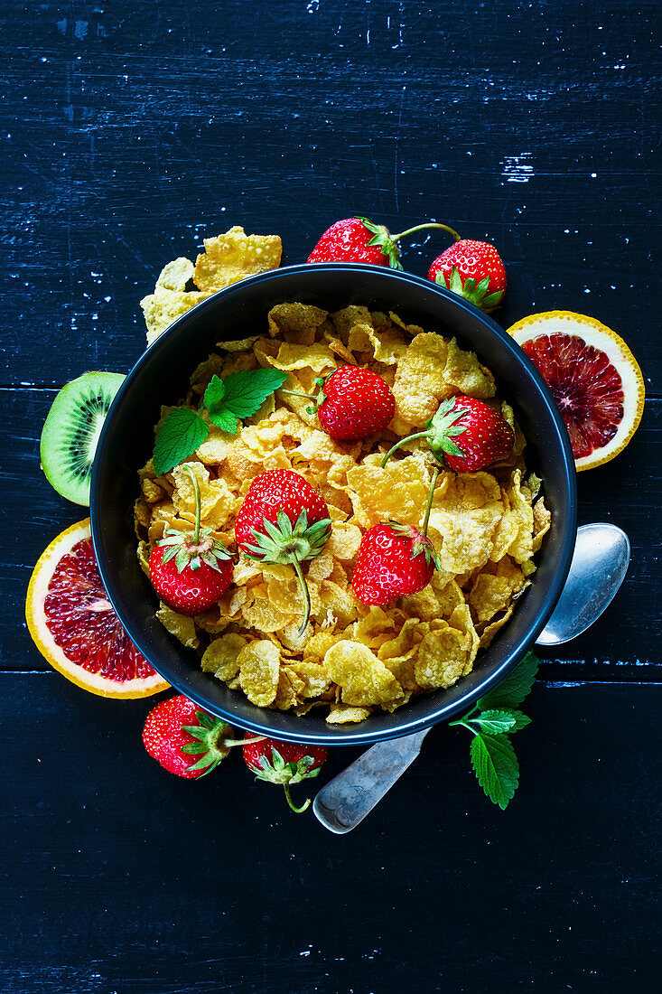 Close up of vintage table with healthy breakfast set. Corn cereal, fresh strawberry and fruits over dark rustic wood backdrop