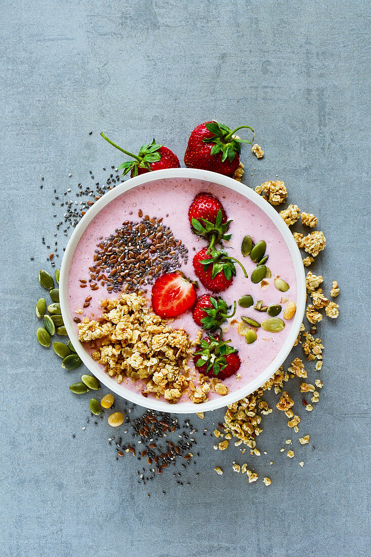 Tasty strawberry smoothie bowl with fruits, cereals, seeds and nuts over light grey background