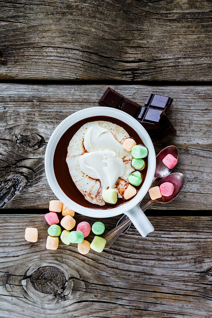 Close up of hot chocolate in white ceramic cup with whipped cream and marshmallows on rustic wooden background