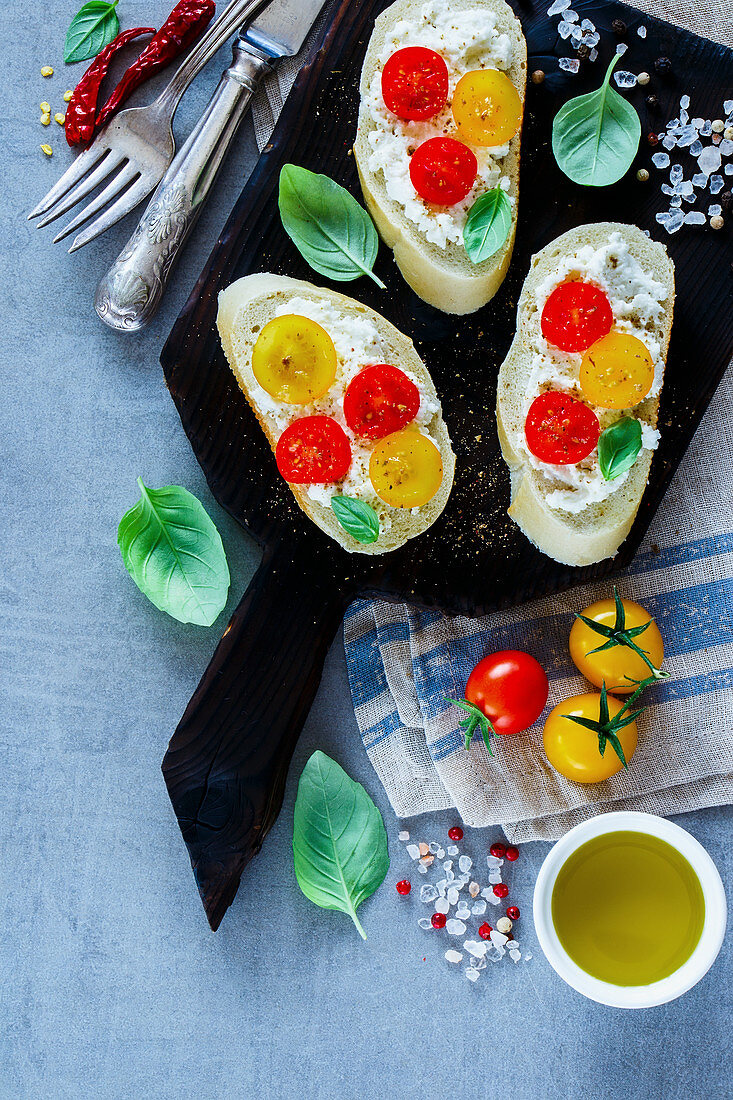 Close up of homemade tomato and basil bruschetta or sandwiches with ingredients on light grey background