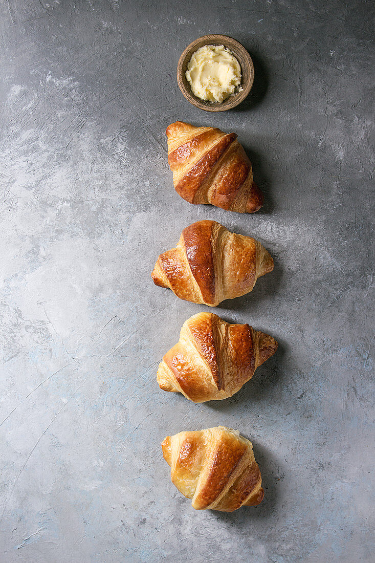 Fresh baked traditional croissant with butter in row over grey texture background
