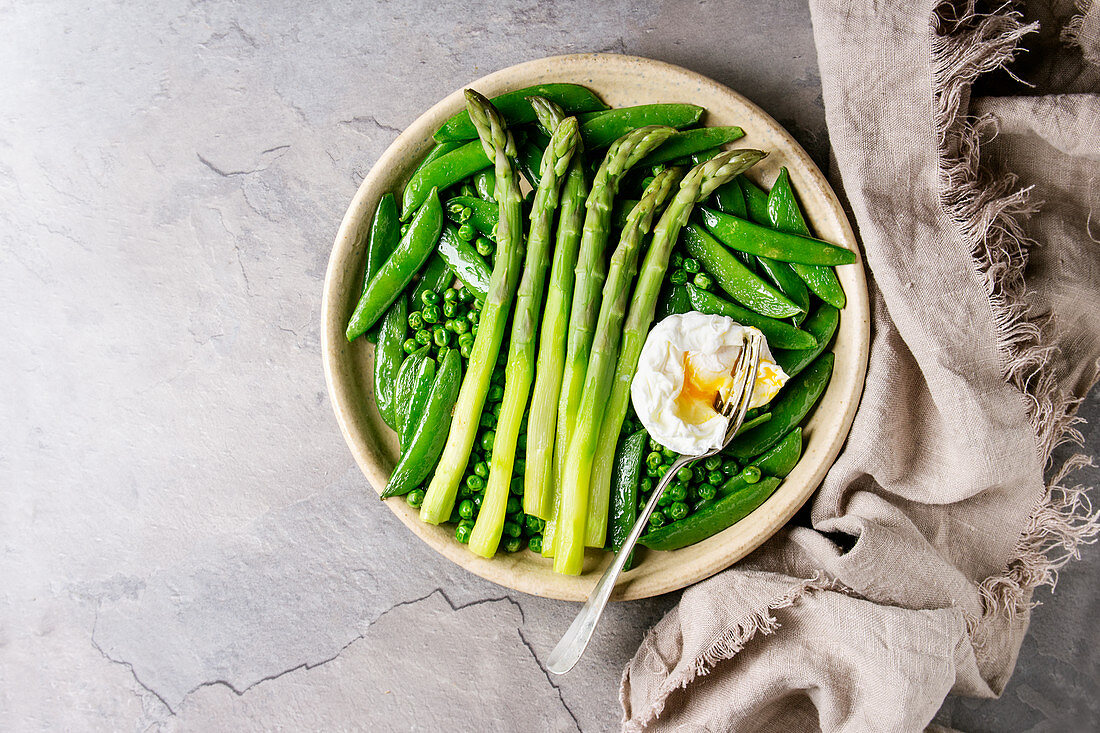 Variety of cooked green vegetables asparagus, peas, pod pea, served with bread and poached egg