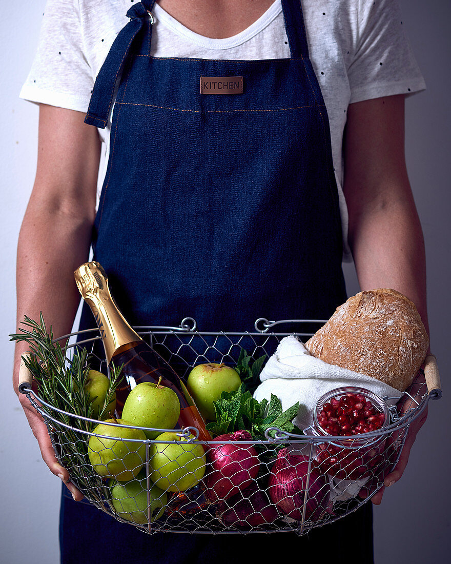 A person holding various groceries in a wire basket