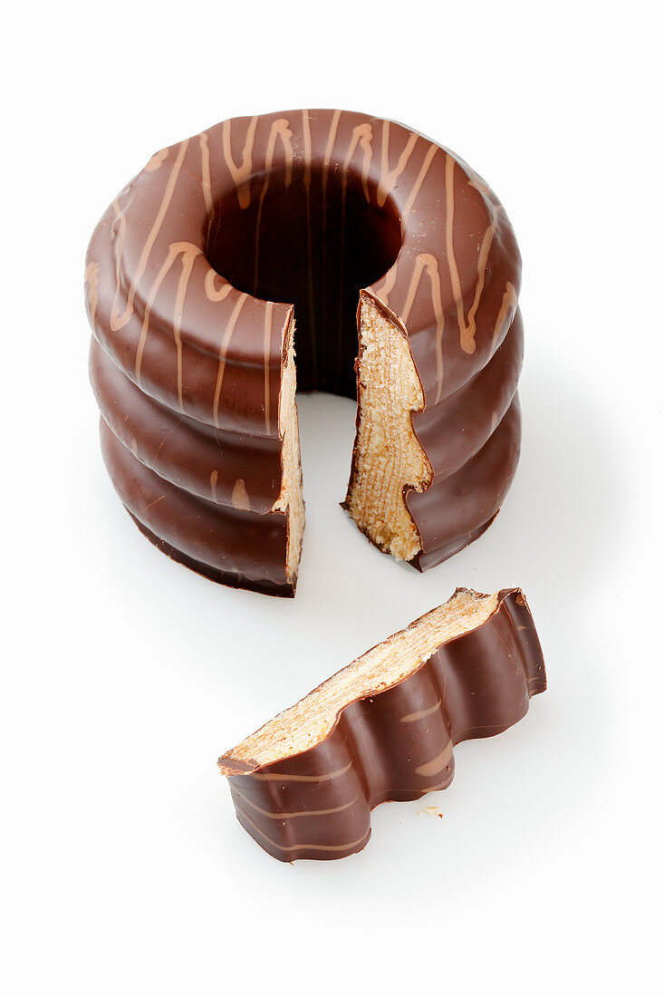 A sliced Baumkuchen (German layer cake) with chocolate glaze on a white surface