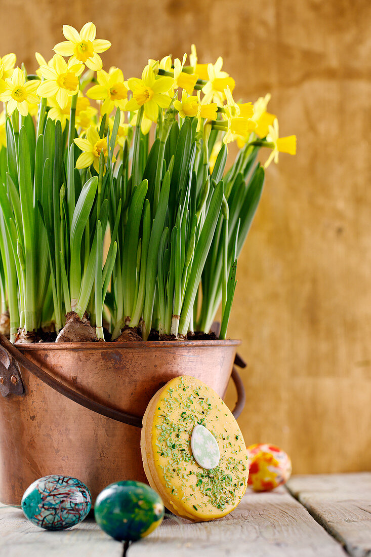 Egg-shaped Hanseatic Easter cake leaning against a copper pot of narcissi
