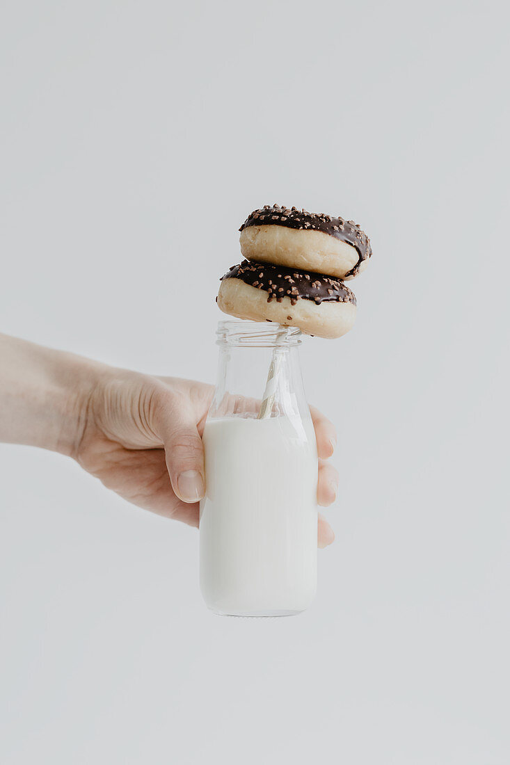 A hand holding a milk bottle with two doughnuts on a straw