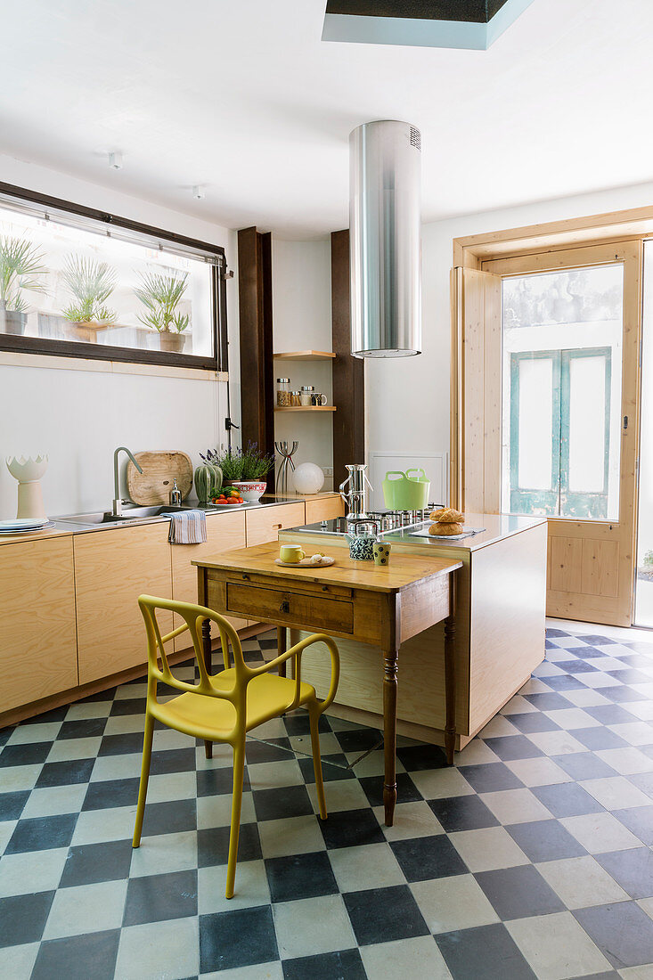 Island counter, kitchen table and yellow chair on chequered floor in kitchen with terrace doors