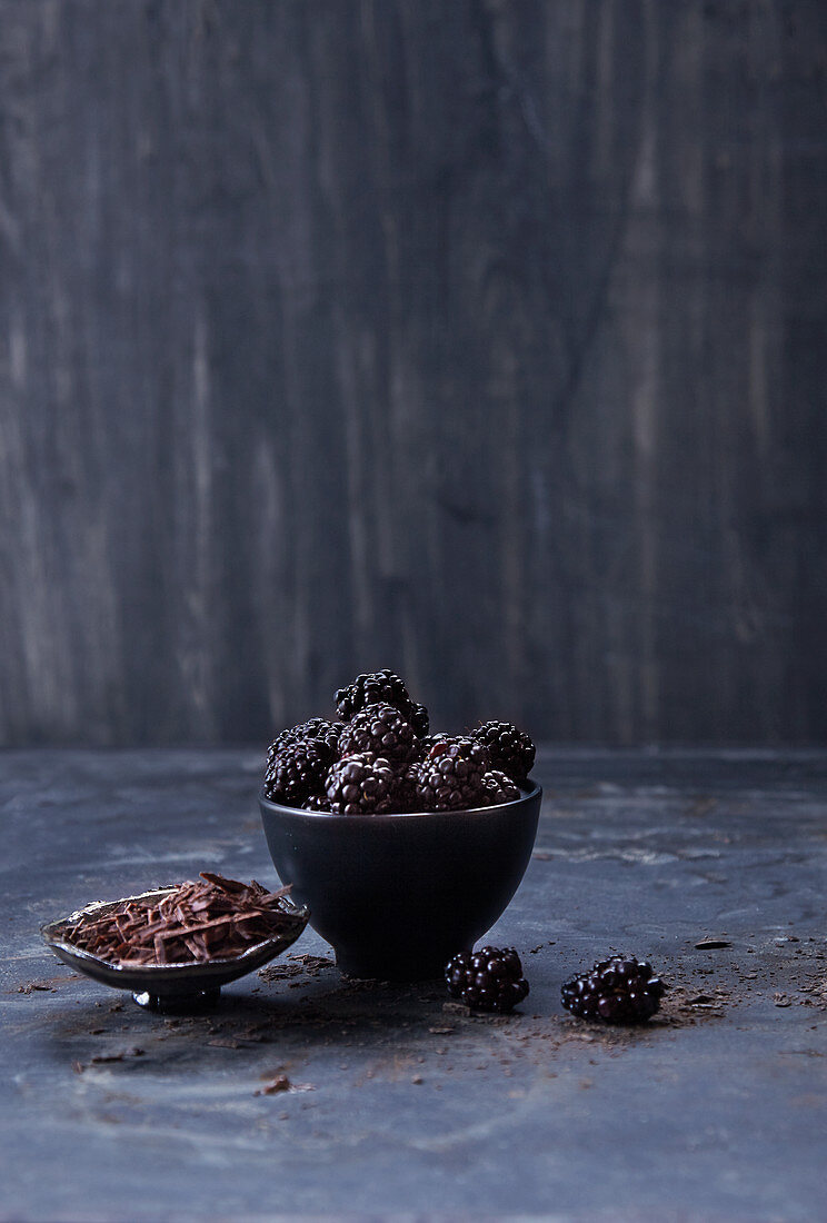 Brombeeren und Schokoladenraspeln in Schälchen vor dunklem Hintergrund