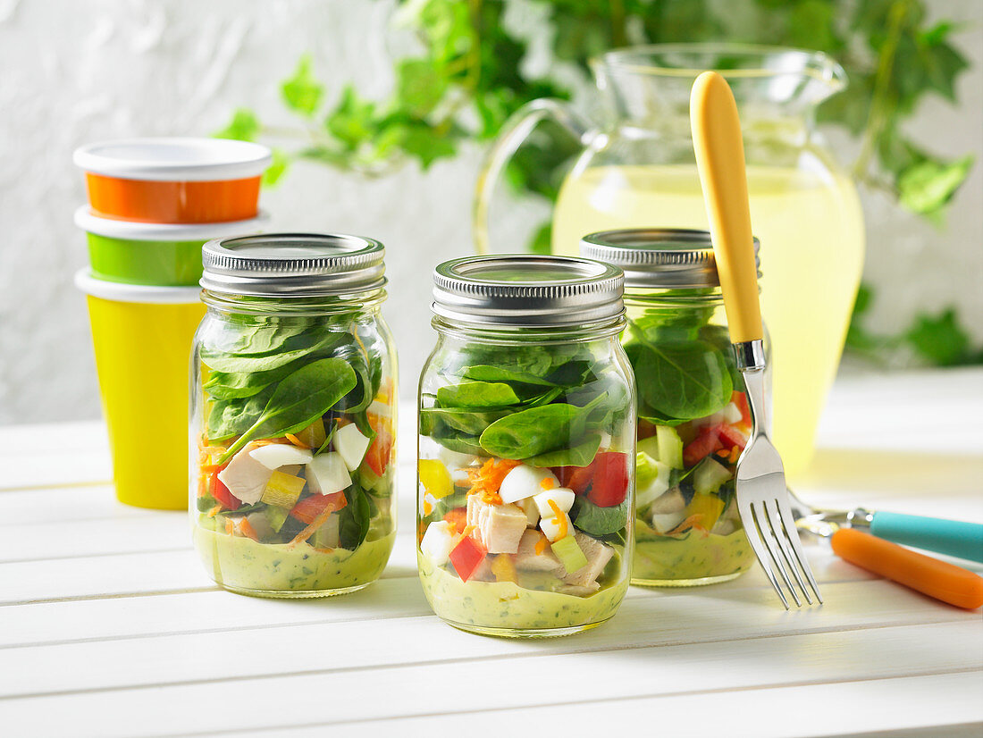 Salad in glass jars with chicken, spinach and eggs