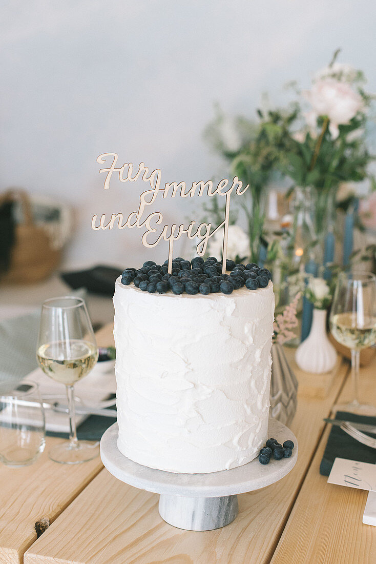 Tortenstecker mit Schrift auf einer hohen Torte mit Blaubeeren