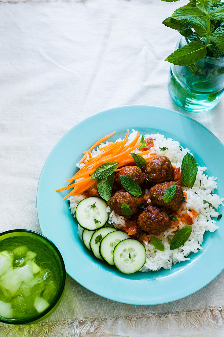 A turquoise plate with meatballs, tomatoe sauce and mint rice, garnished with slices of cucumber and carrots