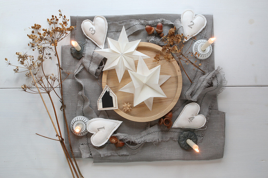 An original Advent calendar with decorative paper stars on a wooden tray and homemade fabric hearts with numbers