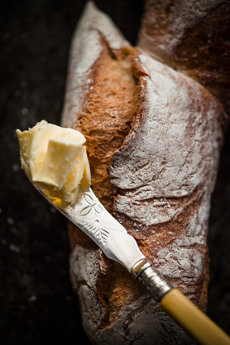 A piece of pain d'Epi (French baguette shaped like an ear of wheat) and a knife with butter