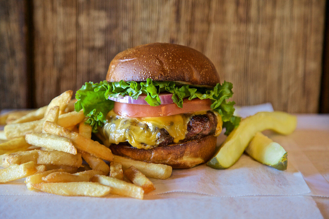 Cheeseburger mit Salat, Tomate, Zwiebel, Essiggurke und Pommes