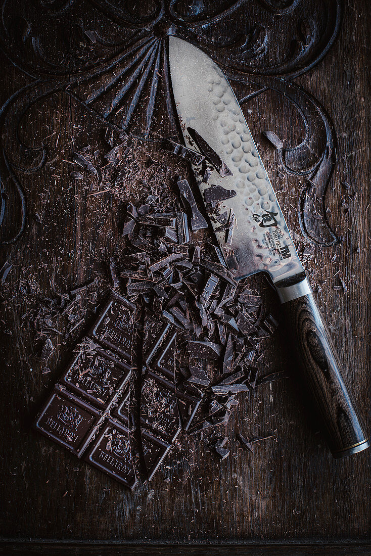 Gehackte Schokolade mit Messer auf Holzuntergrund (Aufsicht)