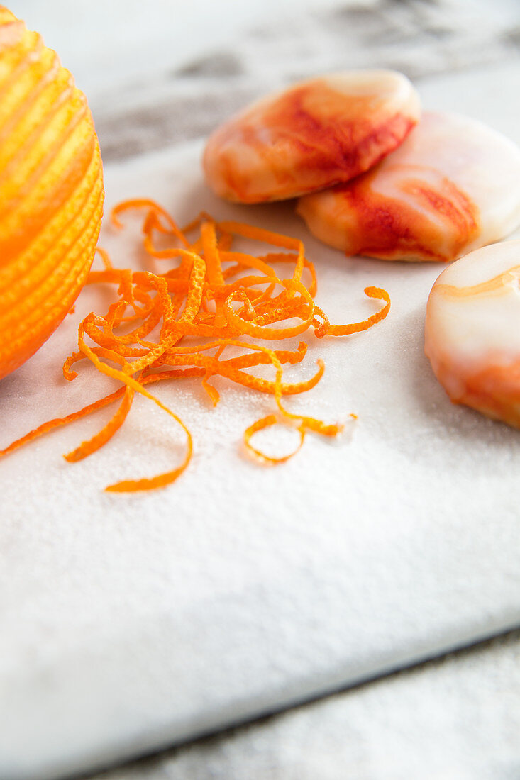Orangenschale neben Orangenkeksen mit marmorierter Orangenglasur (Nahaufnahme)