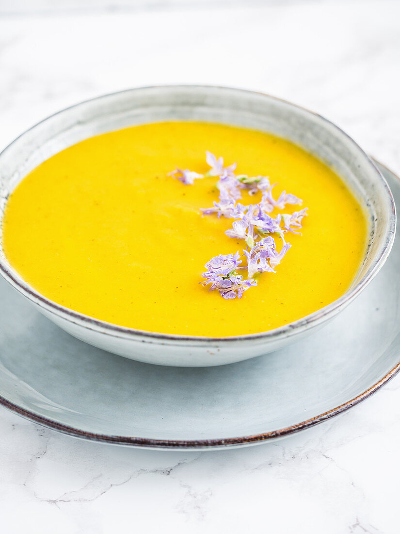 Vegan pear, carrot and pumpkin soup, served with edible rosemary flowers