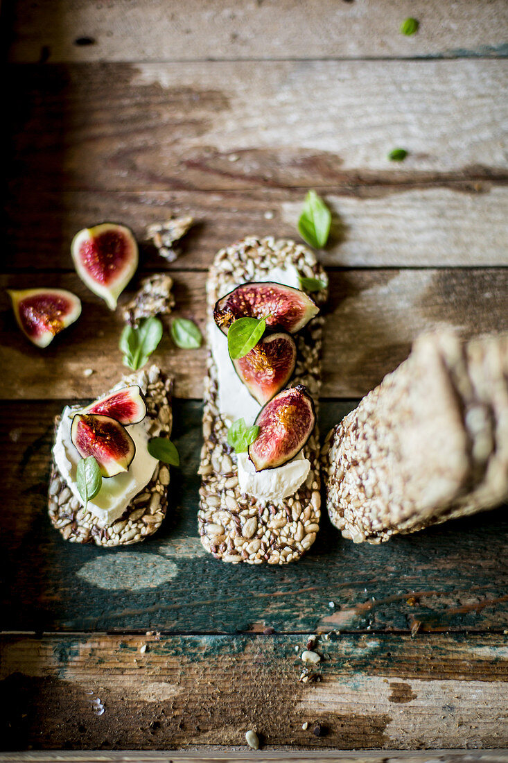 Low carb seeded crackers, figs, cream cheese and basil on a rustic wooden surface