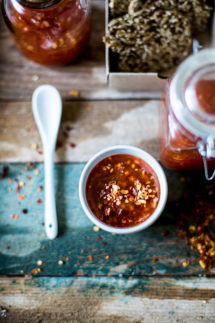 Festive sweet chili sauce in a jar with crackers served as a gift on a rustic wooden surface with a green name tag