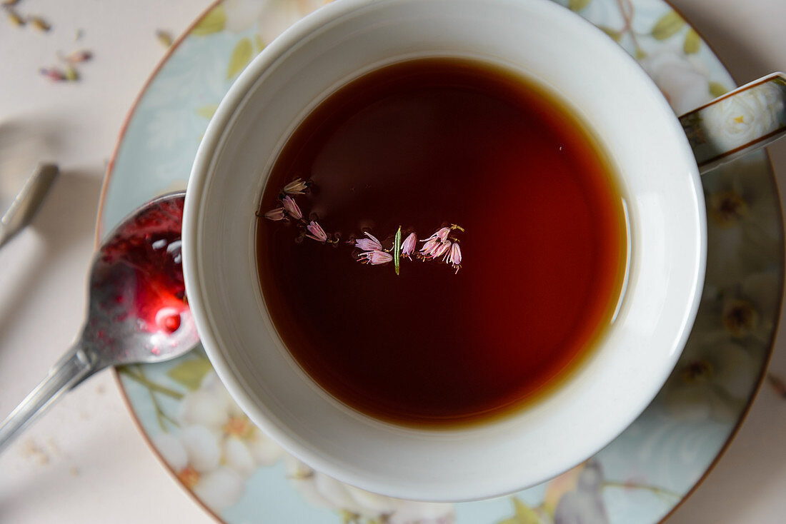 A cup of black tea with herbs, a spoon with red jam